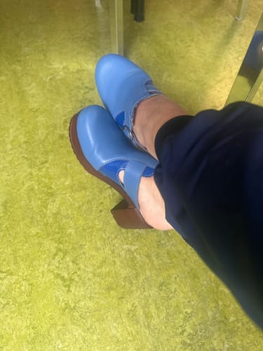 Customer resting their feet while wearing the blue leather Sonja Blue clogs with a wooden heel.