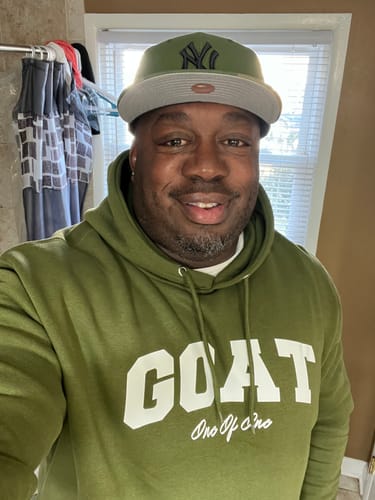 Reviewer smiling in an olive green Goat Hoodie with a white logo on the chest.