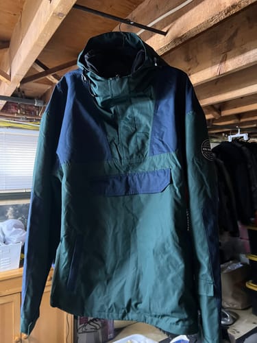 Customer's color-block snow anorak in green and blue, hanging on a hanger indoors.