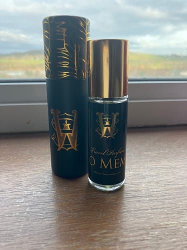Customer's Ko Mem travel perfume bottle and its matching black case with a gold-patterned lid on a wooden surface.
