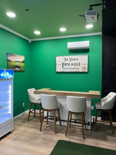 Customer's 19th Hole Golf Personalized Sign hanging over a bar in a golf simulator room with green walls.
