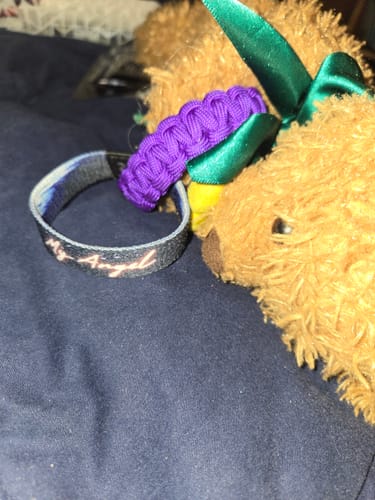Reviewer's My Angel Bracelet on a dark surface next to a purple bracelet and a teddy bear.
