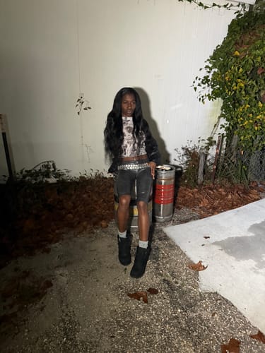 Reviewer sitting outdoors at night wearing the black Leather Capris with a studded belt and boots.