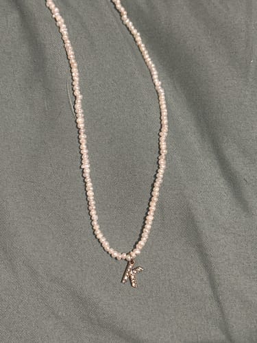 Customer's Shelly Crystal Pearl Initial Choker with a sparkling 'K' pendant laid on a gray surface.