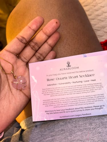 Customer holding a pink rose quartz heart necklace in their palm next to its descriptive card.
