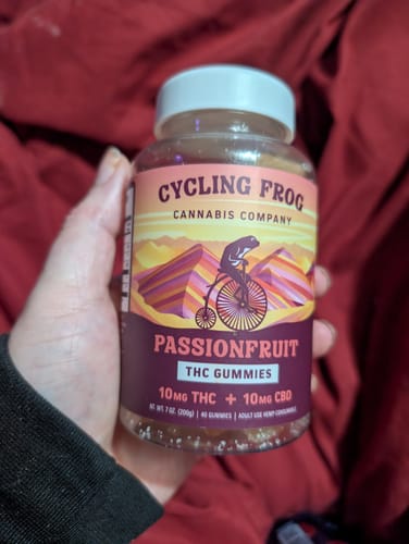 Customer's hand holding a bottle of Passionfruit Gummies against a red background.