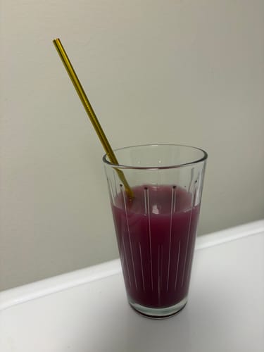 Customer's prepared Berry Kava Drink Mix, a purple liquid in a ribbed glass with a gold straw.