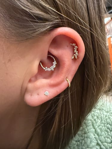 Customer's curated ear showing the gold Eternity Pavé Clicker sparkling in a helix piercing among other earrings.