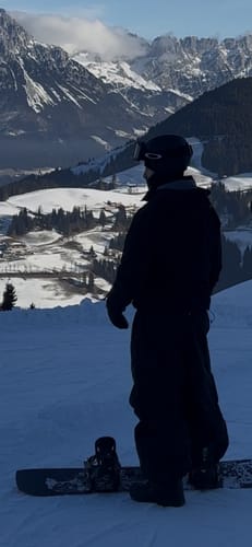 Reviewer wearing the baggy black snow pants on a snowy mountain with a snowboard.