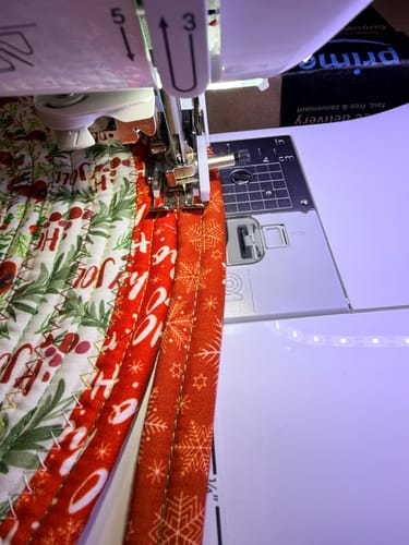 Close-up of a customer's Baby Lock Jubilant sewing machine stitching the red binding on a holiday-themed project.