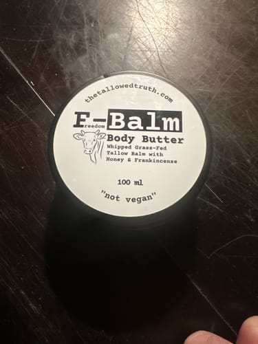 Customer's overhead view of the F-Balm Whipped Body Butter tin, showing the product label on a dark surface.