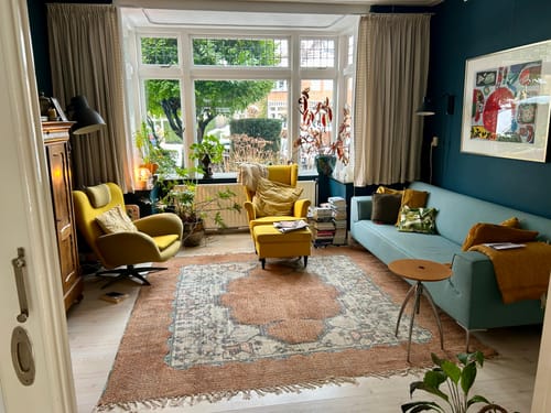 Recensent toont het vierkante HKliving Printed Rug vloerkleed in een kleurrijke woonkamer.