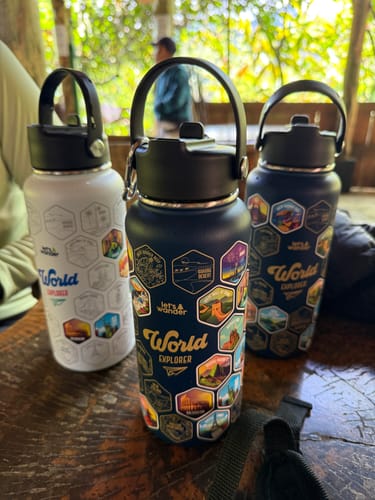 A reviewer's dark blue and white World Explorer Water Bottles shown with colorful travel stickers on a table.
