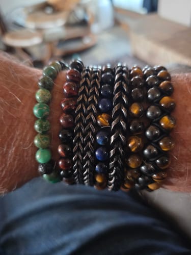 Reviewer wearing the Phoenix Rising bracelet with fire agate and lava beads as part of a large bracelet collection on their wrist.