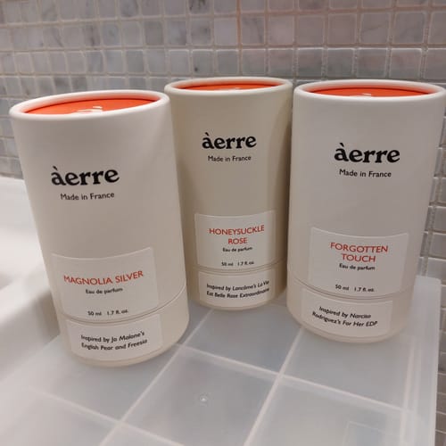 Customer's Honeysuckle Rose perfume in its white cylindrical packaging, placed with two other similar products on a counter.