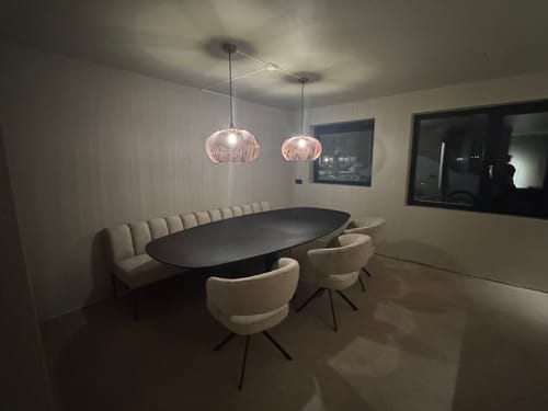 Klantfoto van twee verlichte, koperen Finn hanglampen die sfeervol boven een ovale eettafel hangen.