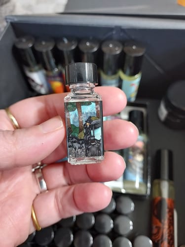 Customer holding a small bottle of Midwinter Dirge perfume oil, showing its illustrative label in front of a collection.
