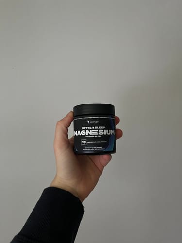 Reviewer holding a small black jar of Complex Sleep Magnesium against a plain background.