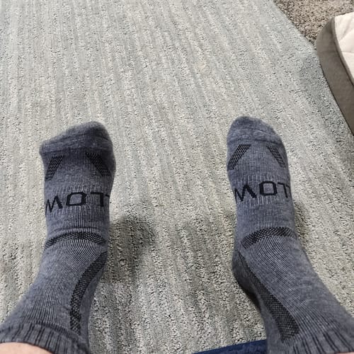 Reviewer's feet wearing the grey Men's Alpaca Socks, showing their snug fit against a carpeted background.