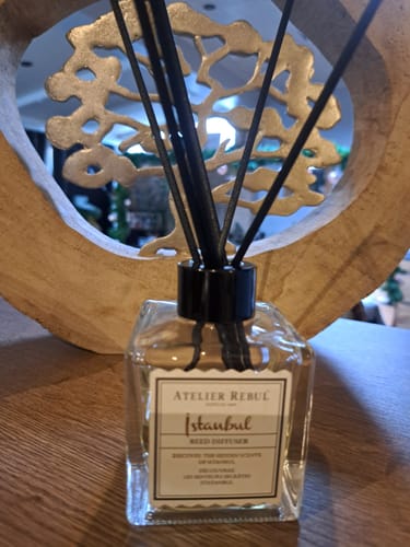 Recensent toont de Istanbul Geurstokjes in het glazen flesje op een houten ondergrond.
