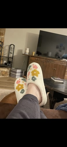 A reviewer relaxes with their feet propped up, wearing the floral Livia Flower Slippers.