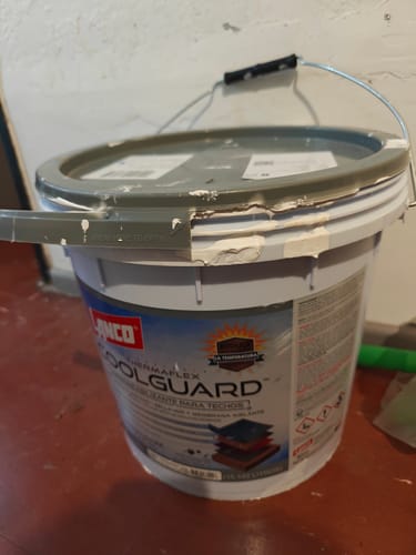 Cliente muestra el cubo usado del sellador de techos Lanco Coolguard sobre un piso rojo.