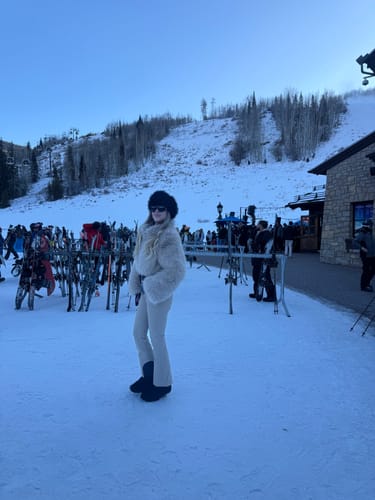 Reviewer wearing the khaki slim-fit ski suit with a faux fur jacket and flared legs in the snow.