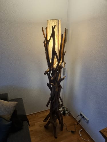 Kunde zeigt seine beleuchtete Treibholz Stehlampe VILLA in einer Zimmerecke.