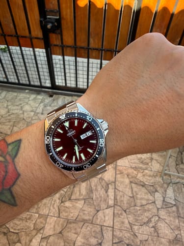 Reseñador muestra un primer plano de su reloj Orient Kamasu en la muñeca, con esfera roja y correa de acero.