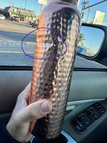 Customer holds the hammered copper water bottle, showing a large dent circled on the side.