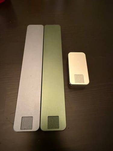 Reviewer's two sleek metal pill cases, one silver and one green, laid out on a dark tabletop.