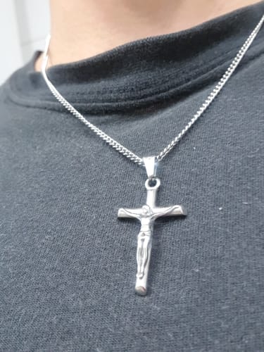 Primer plano del Colgante Cross Minimal de un cliente, un crucifijo plateado que lleva sobre una camiseta oscura.