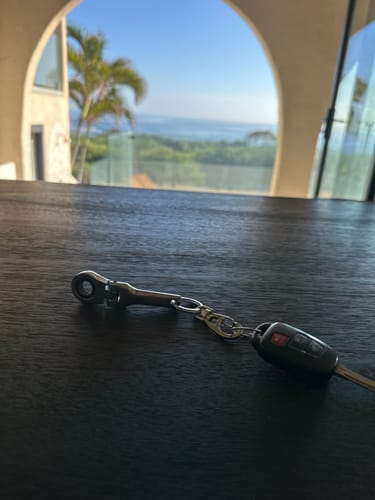 Reviewer's 10mm Wrench Keychain attached to a car key on a dark wood table with a scenic ocean view in the background.
