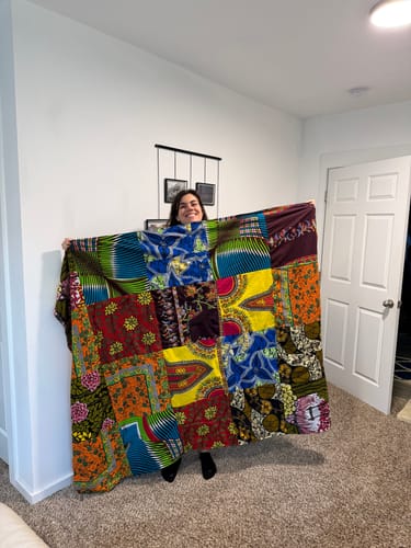 Reviewer smiling while holding up their large T-Shirt Quilt made from vibrant African fabrics.
