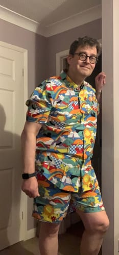 Reviewer standing indoors wearing the Disney "Dreamland Drip" Hybrid Shorts with a colorful matching shirt.