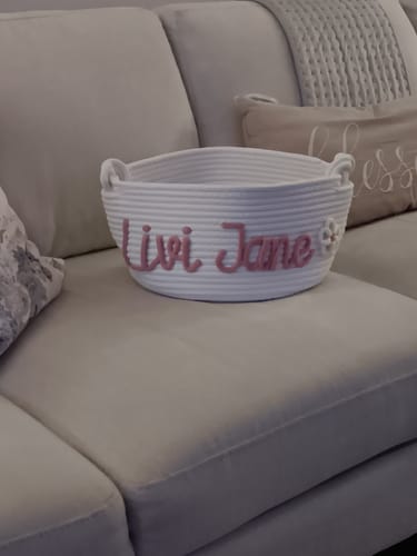 Customer's personalized white basket with the name 'Livi Jane' in pink, sitting on a couch.