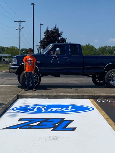 Customer wearing the orange HEATER TEE while standing next to a large truck in a parking lot.