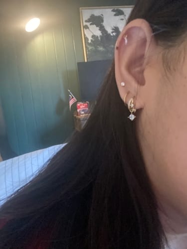 Reviewer shows the gold Eclipsa Illusion Huggies with a dangling charm worn in their ear lobe.