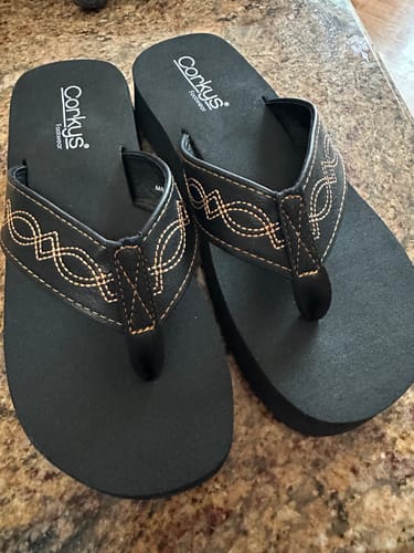Customer's pair of black Corky's Overboard Sandals with tan stitching on a countertop.