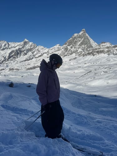Reviewer wearing the baggy black snow pants while standing in deep snow on a mountain.
