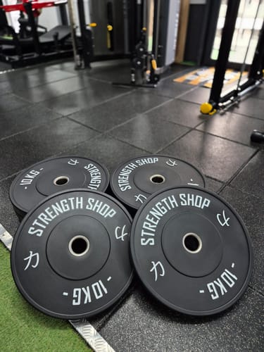 Customer's four black 10kg Riot Bumper Plates lying on a rubber gym floor.