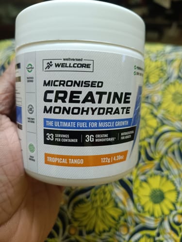 Customer holding a white tub of Wellcore's Micronised Creatine Monohydrate in Tropical Tango flavor.