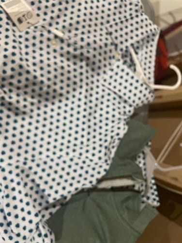 Partial view of a customer's white Shamrock Men's Polo with a green pattern on a hanger, over a green shirt.