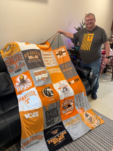 Customer proudly holding up a large Premium T Shirt Quilt made from orange and grey Tennessee Volunteers t-shirts.