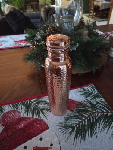 Customer's hand-hammered copper water bottle standing on a dining table with a festive snowman placemat.