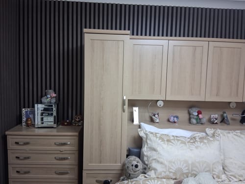 Customer's dark Premium Acoustic Slatted Wall Panels installed as an accent wall in a bedroom with light wood furniture.