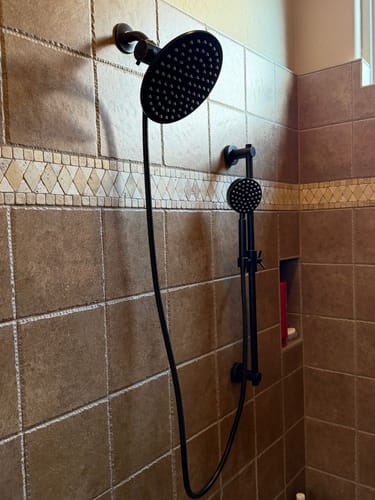 Customer's black dual shower head with adjustable arm installed in a brown tiled shower.