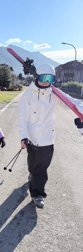 Customer wearing the black Baggy Snow Pants and a white jacket while carrying skis on a paved road.