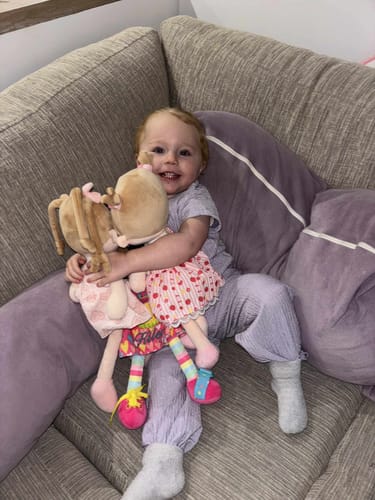 Customer's smiling child sitting on a couch and hugging their Personalized Strawberry Girl doll.