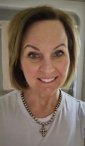 Customer wearing the Tova Baby Donatella Necklace. The cross pendant with caramel crystals stands out against a white t-shirt.